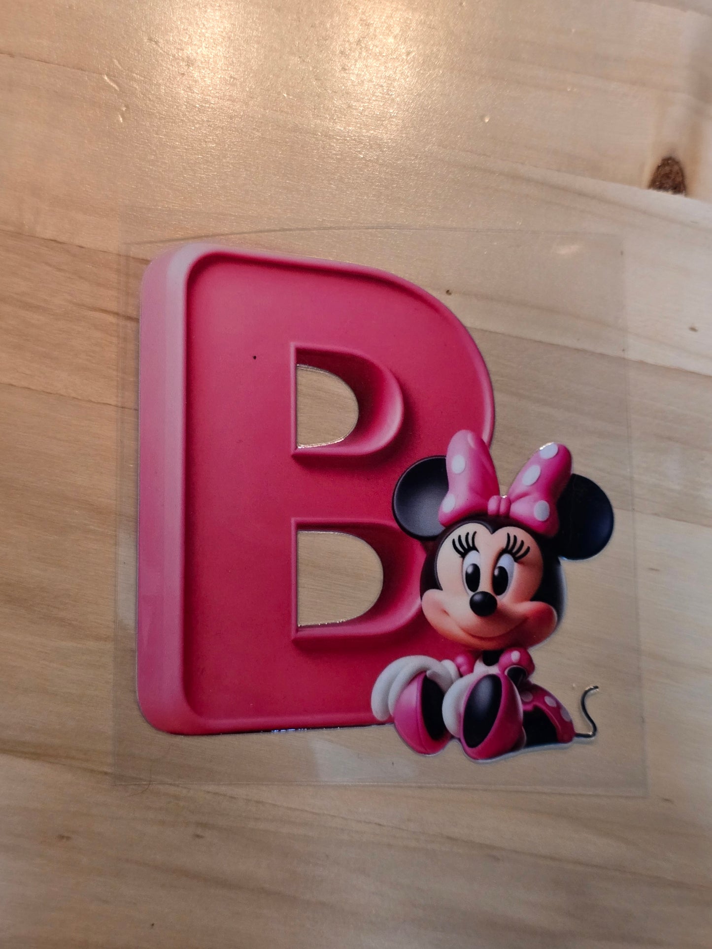 Pink letter 'B' with a cartoon character on a wooden surface